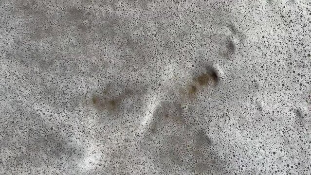 sea wave washes away two footprints steps on the sand, vertical footage.