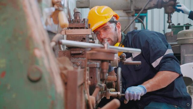 Young caucasian engineer man operating lathe machine for preparing production at factory industrial, technician or labor maintenance machinery at workplace, metalworker working, industry concept.