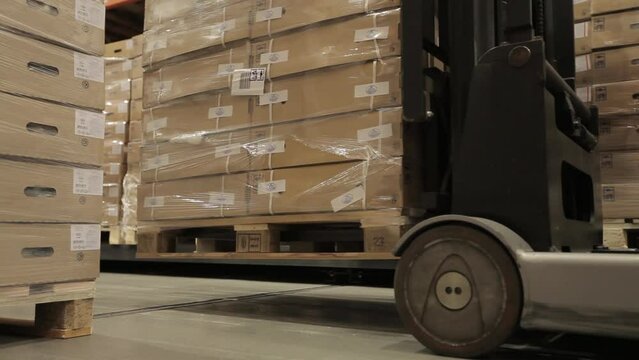 Forklift in a logistics warehouse picks up pallets of product from the floor. A general layout of pallets and boxes on the floor