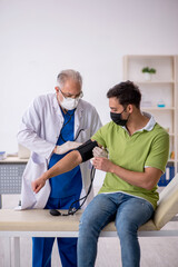 Obraz premium Old male doctor measuring young patient's blood pressure