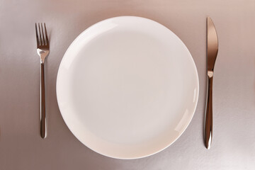White plate with fork and knife on gray background.