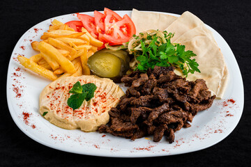 Dinner fried beef with french fries, chickpea puree, tomatoes, pickles, greens and pita bread.