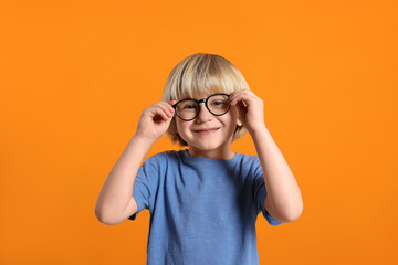 Cute little boy wearing glasses on orange background