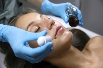 Obraz na płótnie Canvas Cosmetologist applying serum on client's face in salon