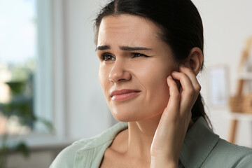 Young woman suffering from ear pain in room, closeup