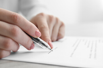 Woman signing documents at wooden table in office, closeup