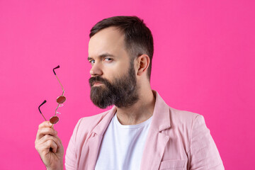 Bearded man dressed in a pink jacket with glasses. Emotional studio portrait.