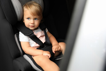 Cute little girl sitting in child safety seat inside car