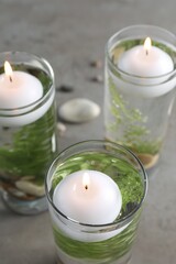 Fototapeta na wymiar Candles, stones and fern leaves in glass holders with liquid on grey table, closeup