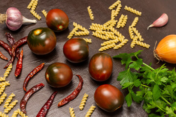 Brown tomatoes, parsley, pasta and dry red pepper pods on the table.