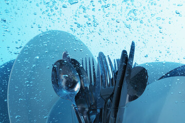 Washing silver cutlery and plates in water on light blue background