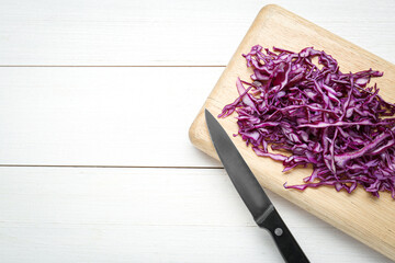 Board with shredded fresh red cabbage and knife on white wooden table, flat lay. Space for text
