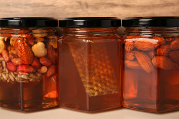 Fototapeta na wymiar Jars with different nuts and honey on light table near wooden wall, closeup