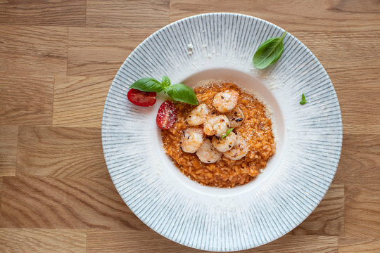 Tomato risotto with shrimps and basil on a wooden table. Top view, selective focus.