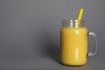 Mason jar of tasty smoothie with straw on grey background. Space for text