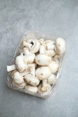 Champignon mushrooms in the plastic box at the grey background