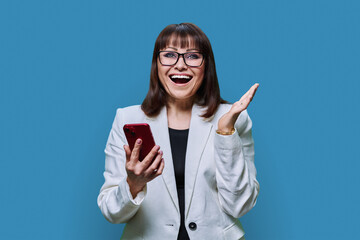 Portrait of surprised middle aged business woman with phone on blue background