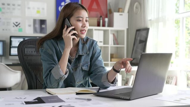 Asian Woman Graphic designer talking on mobile phone while working in office. Artist Creative Designer Illustrator Graphic Skill Concept.