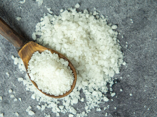 Fototapeta na wymiar sea salt, a pile of sea salt in a wooden spoon on a dark stone background close-up