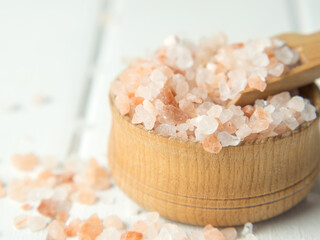 Fototapeta na wymiar pink sea salt, heap of sea salt in a wooden bowl and scoop on a light wooden background close-up