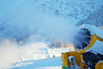Snow cannon in winter mountains. Snow-gun spraying artificial ice crystals. Machine making snow