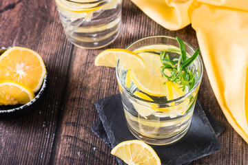 Pieces of lemon in a glass of water and rosemary on a wooden table. Detox drink