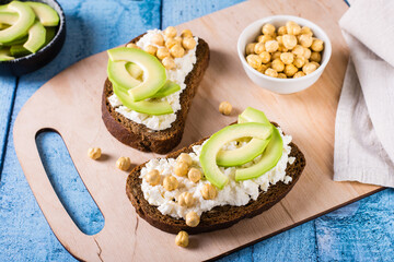 Bruschetta with ricotta, avocado and chickpeas on rye toast on a board. Healthy food.