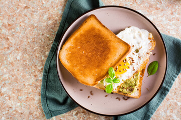 Sandwich with avocado, fried egg and flax seeds on toast on a plate on the table. Top view. Closeup