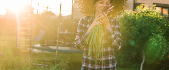 Banner female gardener sniffs bunch of green onions on sunny warm spring day copy space. Plant care...