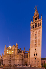 Fototapeta na wymiar The tower of the Giralda Cathedral in the city centre of the Seville during blue hour and sunrise, with the iconic orange fruit trees and the awesome ornaments on the facade of the church.
