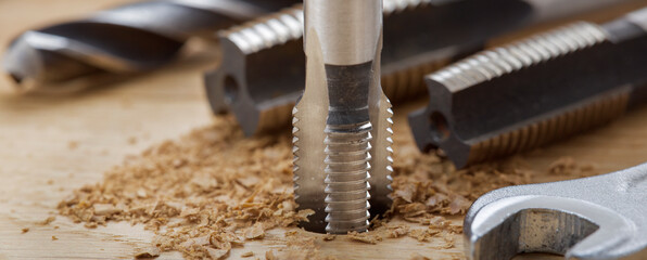 Thread tap drill cutting hole in wooden plate. Working cutter.