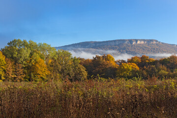 Fototapeta premium Autumn morning in a mountainous area, a panorama of mountains in a blue haze and the rising sun.