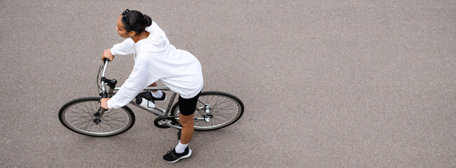 Overhead view of fit african american woman in hoodie cycling on road on street, banner shot 