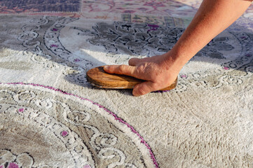 Housewife scrubbing and washing carpet outside with wood brush and soapy water, on a sunny day.