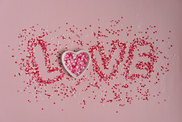 Holiday card concept for Valentine's day. The word "Love" from multi-colored confectionery sprinkles in the form of hearts on pink. Horizontal valentine's day background.