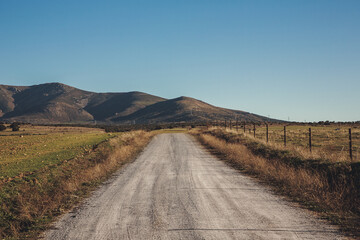 Rural dirt road between agricultural fields against the backdrop of mountains.