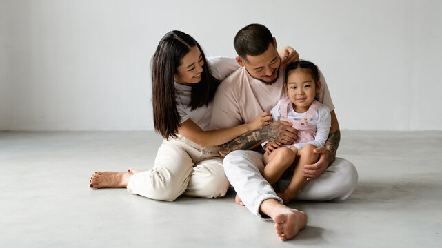 Banner image of smiling barefoot asian parents and toddler child sitting on grey background