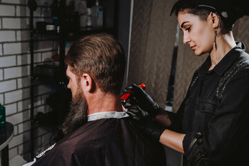 Bearded man getting haircut by hairdresser with dangerous razor at barbershop