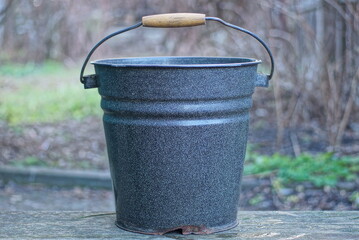 one black old metal enamel bucket stands on a gray wooden table in the street © butus