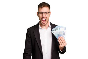 Young business caucasian man holding euro banknotes isolated cut out screaming very angry and...
