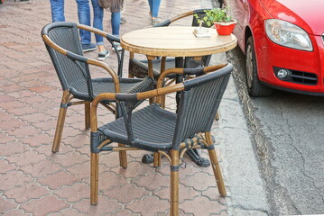 a brown wooden table and black wicker chairs stand on the  pavement of a summer cafe by the road on a city street