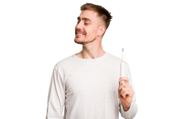 Young caucasian man holding an electric toothbrush isolated cut out looks aside smiling, cheerful and pleasant.