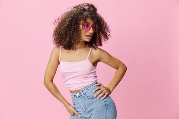 Happy woman afro curls hair dancing on a pink background in summer pink t-shirt jeans and glasses, summer vibe, copy space