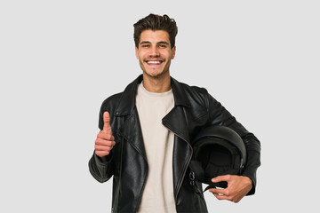 Young caucasian man holding a motrbike black helmet isolated smiling and raising thumb up