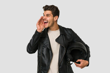 Young caucasian man holding a motrbike black helmet isolated shouting and holding palm near opened mouth.