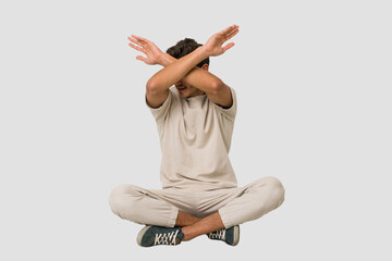 Young caucasian man sitting on the floor isolated on white background keeping two arms crossed, denial concept.