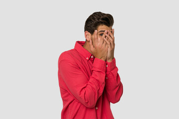 Young handsome caucasian man isolated on white background blink through fingers frightened and nervous.