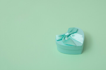 Green heart shape decorative gift box with bow on mint green background. Valentine's day, love,...