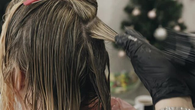 Colorist dyes hair with a brush - a comb to a woman in a beauty salon. Close-up.
