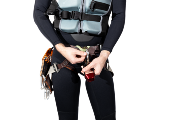 Man wearing a black wetsuit with a life jacket and climbing harness for canyoneering with a rappel device in hand isolated on a white background. Climbing harness with quickdraws and carabiners. 